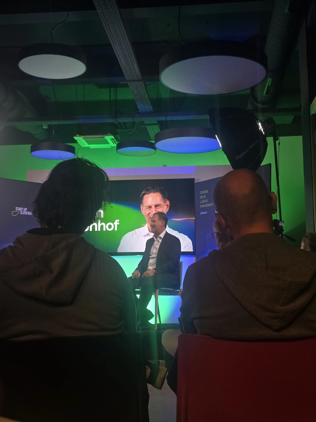 My view past two audience members toward John Denhof seated on stage at Startup Talk in Maribor